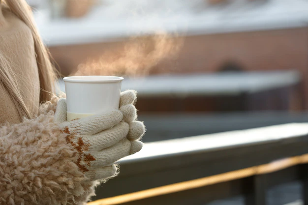 manos-mujer-guantes-blancos-sosteniendo-humeante-taza-blanca-cafe-o-te-caliente-dia-soleado-invierno-frio_165285-2260